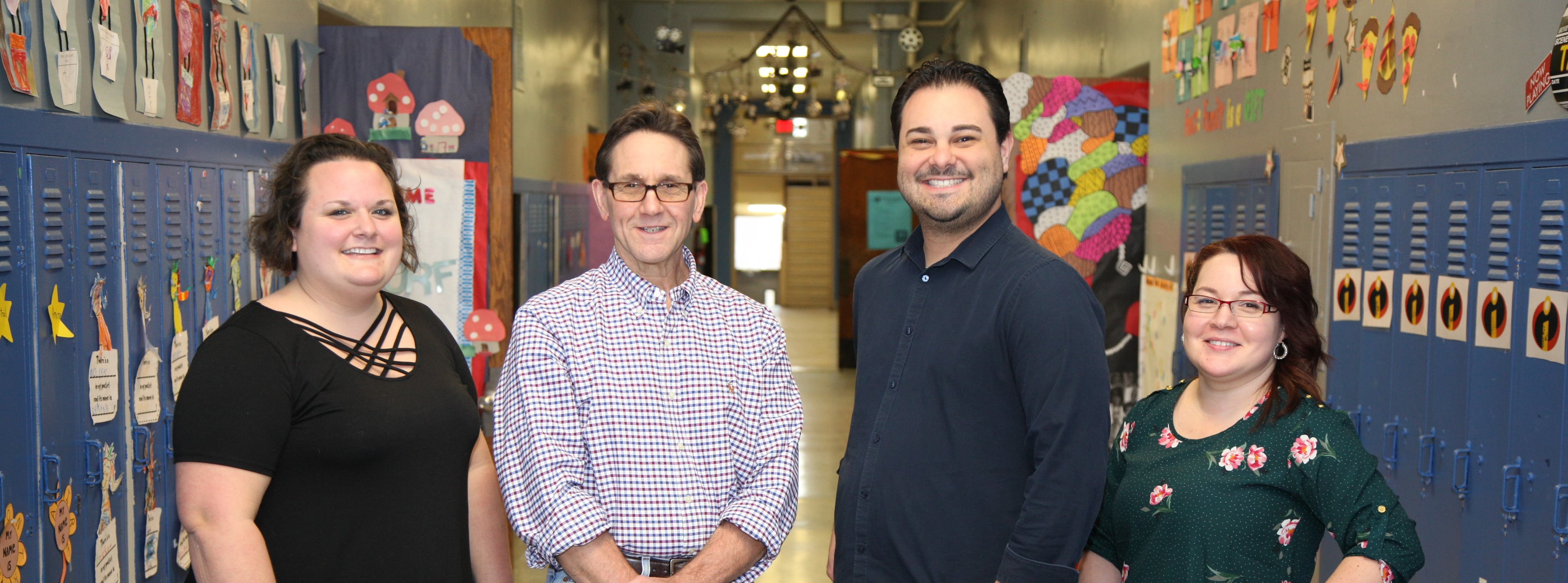 Four smiling adults in a school hallway.